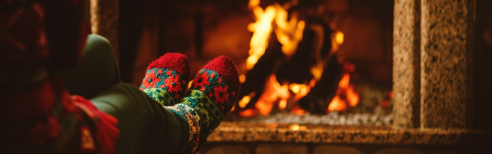 someone with woolen socks warming their feet by a fireplace